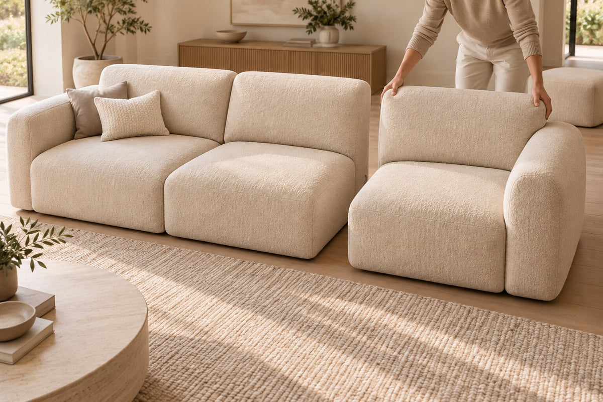 Canapé modulable beige dont un module est déplacé à la main dans un salon lumineux